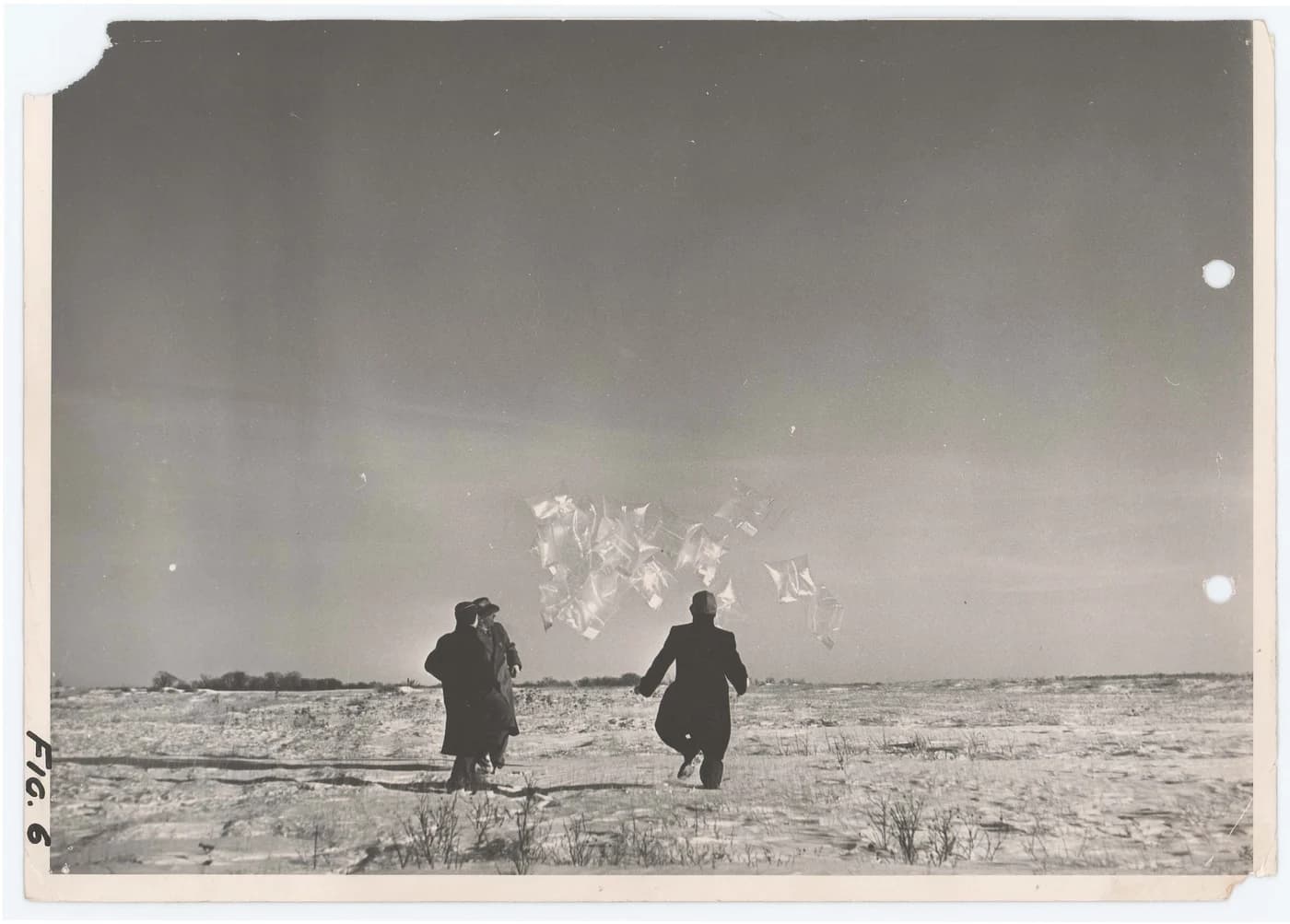 Foto en blanco y negro rotulada «Fig. 6»: tres hombres con abrigo en un campo nevado sueltan un racimo de globos planos y translúcidos.
