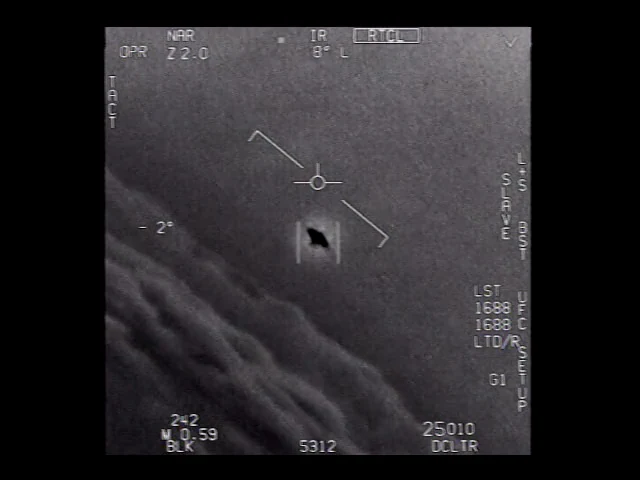 Pantalla infrarroja: un objeto oscuro, inclinado, entre corchetes y con un halo claro.